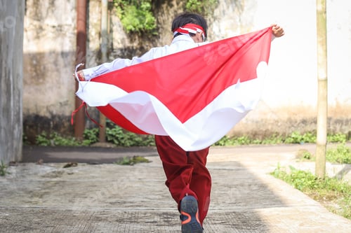 Preview: Rear view of Indonesian student running and hoisting Indonesian flag celebrating independence day.
