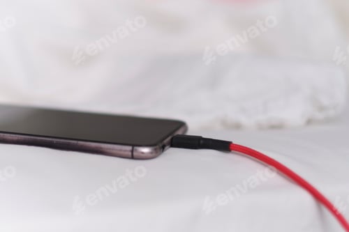 Preview: Smart phone is charging on the bed and lying on white fabric.