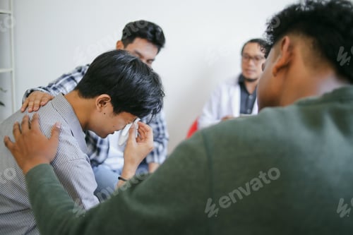 Preview: Portrait Of Young Man Crying and Friends Helping During Group Therapy Session