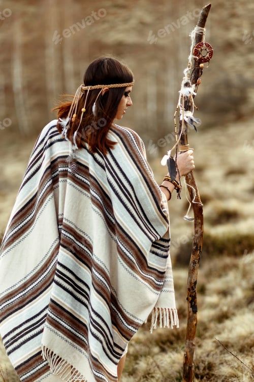 Preview: beautiful native indian american woman holding pikestaff and walking in mountains in evening