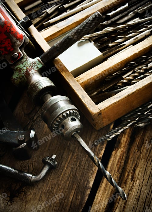 Preview: Old drill, a box with drills, pliers and ruler on wooden background.