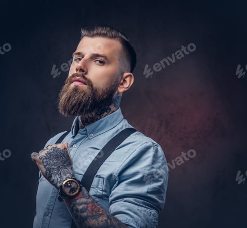 Preview: Portrait of a handsome old-fashioned hipster in a blue shirt and suspenders, posing in a studio.
