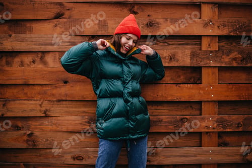 Preview: Fashionable girl in great mood posing on wooden background. Woman in baggy jeans, emerald coat and