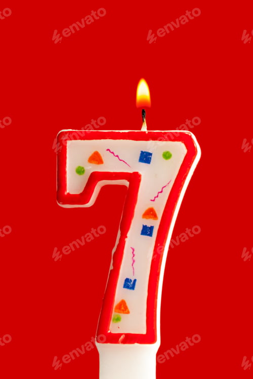 Preview: Bright birthday candle shows the number seven with colorful decorations on a red background