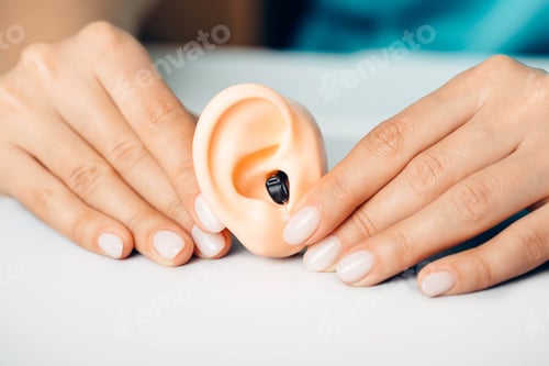 Preview: Doctor showing how to wear a hearing aid using a human ear model.