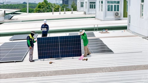 Preview: A technician in safety gear inspects solar panels on a metal rooftop