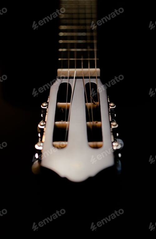 Preview: Vertical closeup of the white headstock of a guitar in the dark