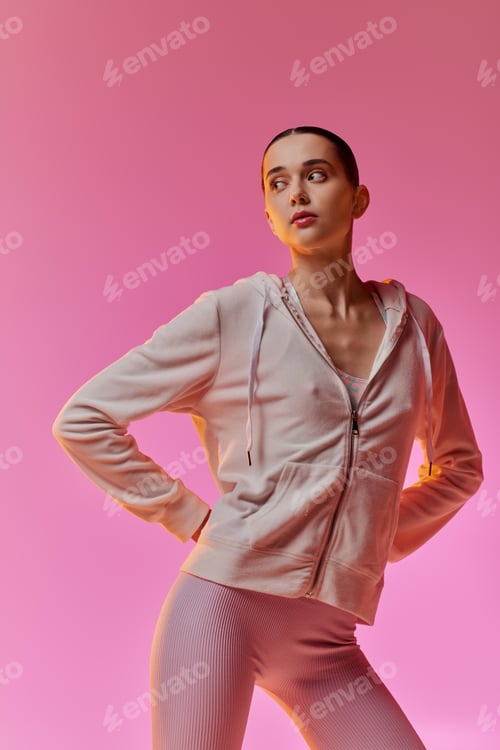 Preview: Stylish young woman poses confidently against a vibrant pink backdrop in comfy activewear