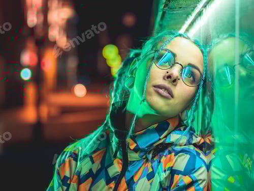 Preview: pretty girl with unusual hairstyle near glowing green neon light of the city at night.Dyed blue hair