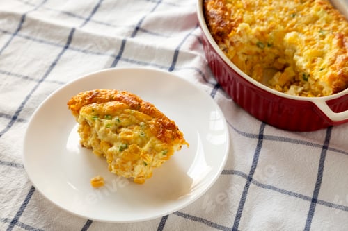 Preview: Homemade Cheddar Corn Pudding Casserole on a white plate, low angle view. Closeup.