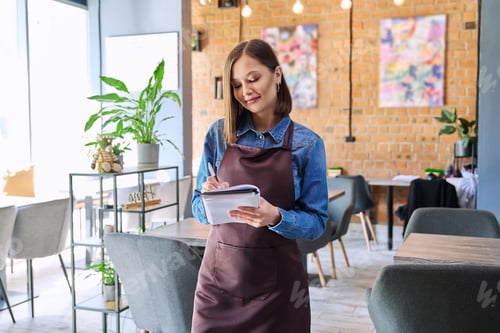 Preview: Young woman worker, owner in apron holding notepad pen in restaurant, coffee shop