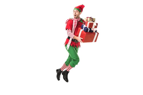 Preview: surprised man in christmas elf costume jumping and carrying pile of presents isolated on white