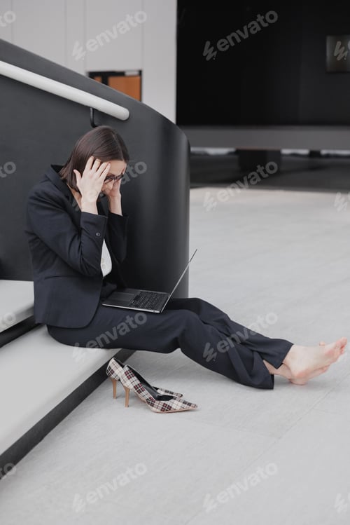 Vista previa: business woman in a formal suit with a laptop in the office is sitting on the steps in stress from