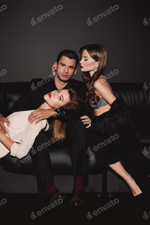 Preview: attractive and stylish women lying and hugging handsome man isolated on black