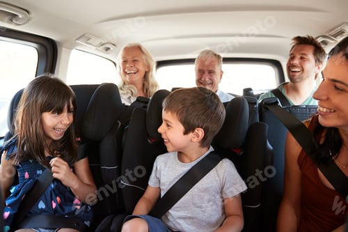 Preview: Three generation white family sitting in two rows of passenger seats in a car, looking at each other