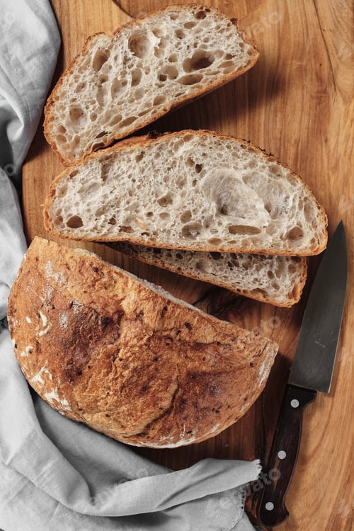 Preview: Sliced loaf of artisan sourdough bread on a cutting board. Top view, vertical frame