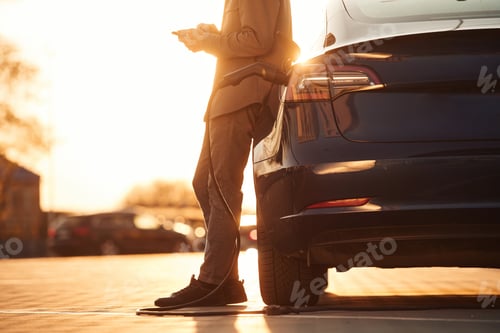 Preview: Bright sunlight. Man is standing near his electric car outdoors
