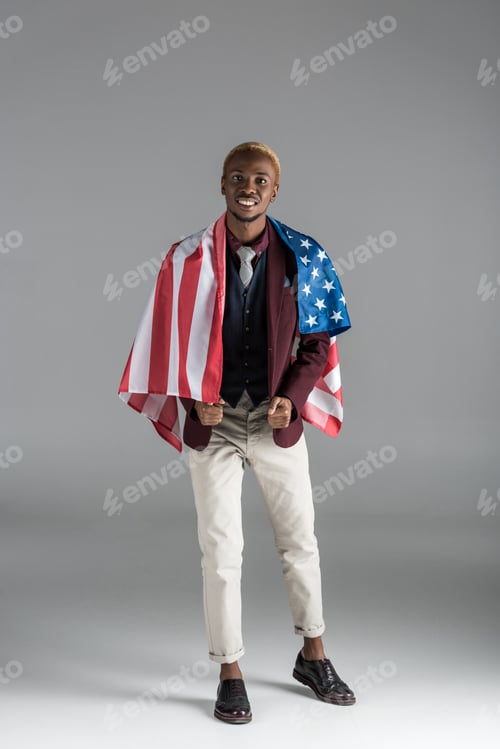Preview: smiling african american man with american flag on shoulders looking at camera isolated on grey
