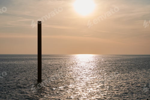 Preview: Large rusty steel construction pillar in blue sea with calm waves at sunset, abandoned building part