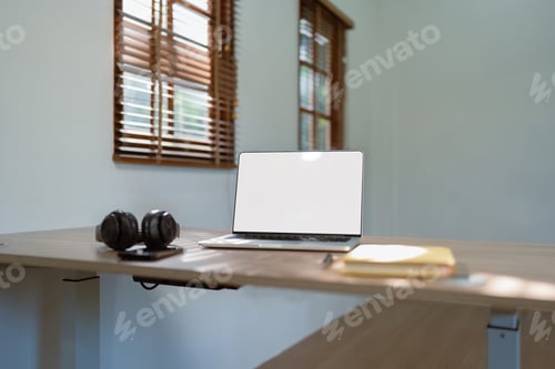 Preview: White screen of laptop, headphones and notebook on the wood table with blurred background of home