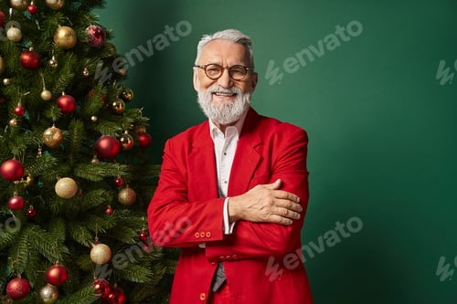 Preview: cheerful Santa in classy red suit with glasses posing next to Christmas tree, winter concept