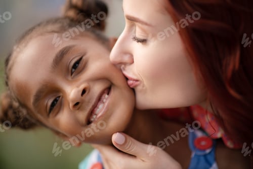 Preview: Adopted girl smiling broadly while mother kissing her