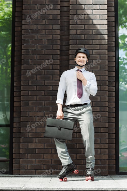 Preview: cheerful roller skater in formal wear fixing tie and smiling at camera near building on street