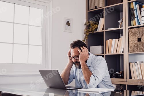 Preview: One alone unhappy and sad man at home in the office using laptop and looking at it