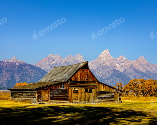 Preview: Wooden house in a green field with a background of a mountain range