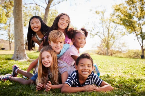 Preview: Multi-ethnic group of kids lying on each other in a park
