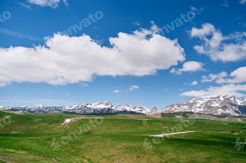 Preview: Hilly green lawn at the foot of the snowy mountains