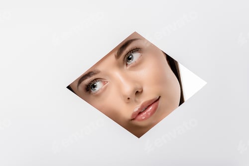 Preview: pensive young woman looking away through rhombus shaped hole on white