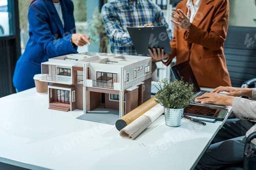 Preview: architect-engineer team discusses modern house model at desk. They review renovation project.