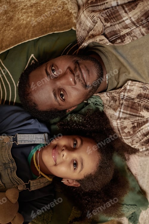 Preview: Portrait of Smiling Black Girl Lying down on Floor next to Dad at Home