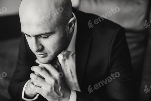 Preview: Contemplative Man in Dark Suit with Folded Hands
