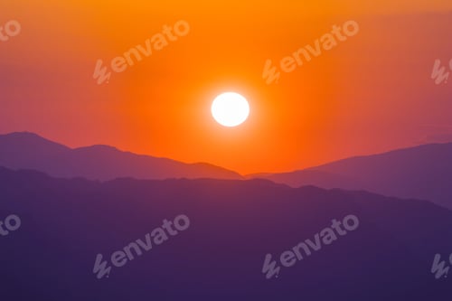 Sun Setting Behind Mountain Ridges in Orange Sky
