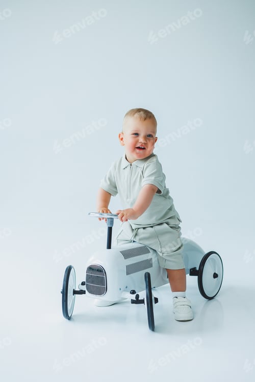 Preview: An adorable toddler joyfully riding a classic toy car in a bright, minimalist studio setting