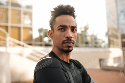 Preview: Close-up portrait of brunet young dark-skinned man in sport black t-shirt looks straight. Serious g