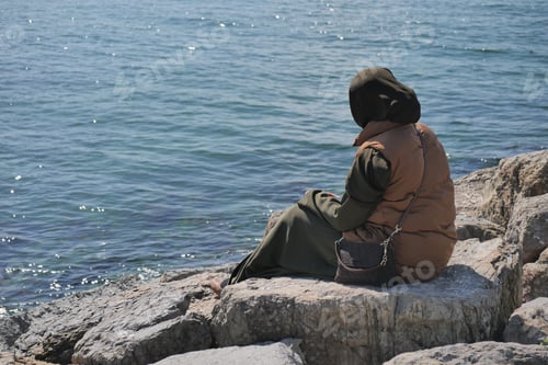Preview: Woman sitting on rocks by the water in daylight
