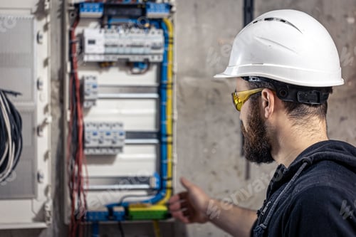 Preview: A male electrician works in a switchboard with an electrical connecting cable.