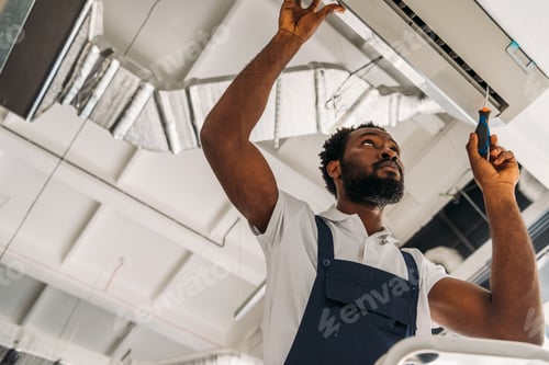 Preview: low angle view of african american handyman repairing air conditioner with screwdriver