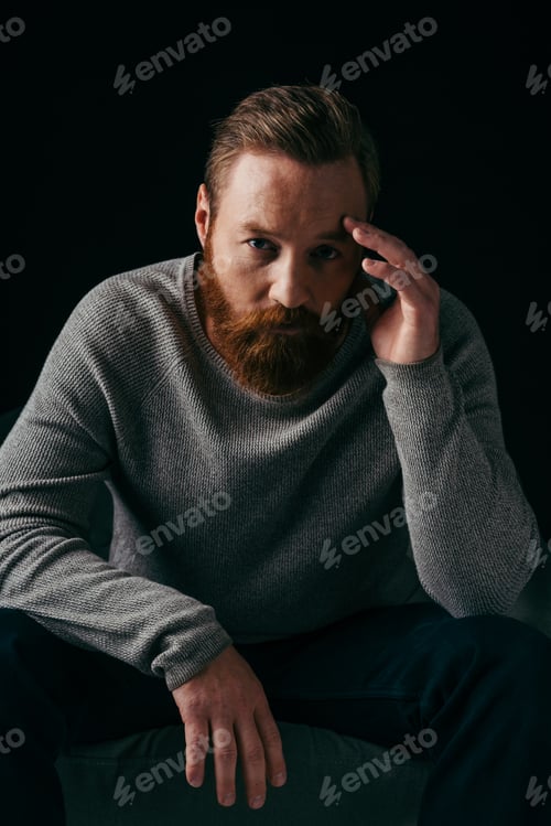 Preview: Portrait of bearded man looking at camera near armchair isolated on black