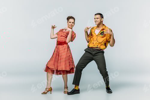 Preview: smiling couple looking at camera while dancing boogie-woogie on grey background