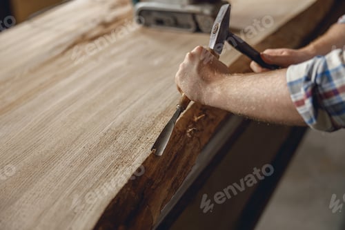 Preview: Close up of craftsman working with chisel while cutting wooden plank in carpentry workshop