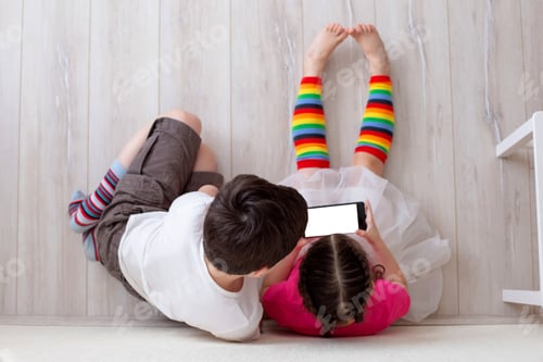 Preview: Two children, boy and girl, are sitting on the floor and playing on a smartphone