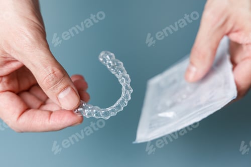 Preview: Man holding transparent aligner and its package. Invisalign orthodontics concept