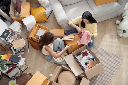 Preview: Asian girl friends unpacking stuff from cardboard boxes at the new house. People moving house