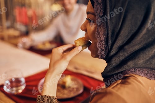 Preview: Close-up of Middle Eastern woman eating baklava at home.