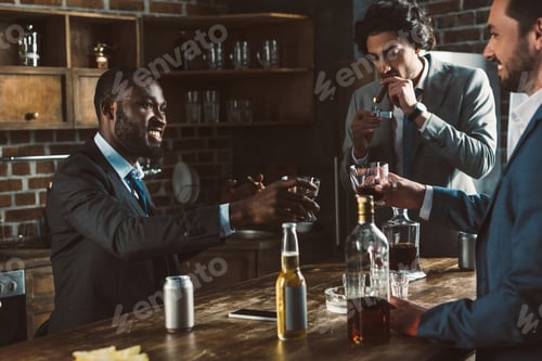 Preview: cropped shot of smiling multiethnic male friends in suits drinking alcoholic beverages and smoking