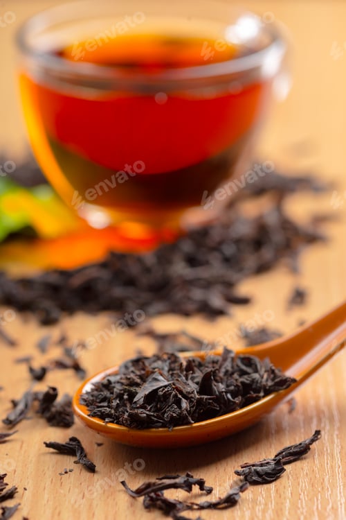 Preview: Black tea leaves and brewed tea in a glass cup on a wooden table